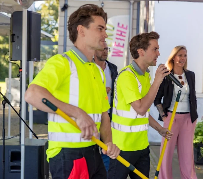 Jim und John moderieren ein Sommerfest, einer mit Mikrofon in der Hand